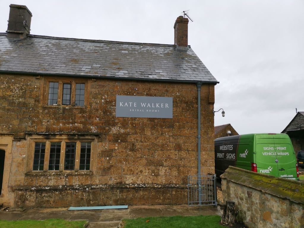 Tray sign of Kate Walker's logo on the side of a stone building