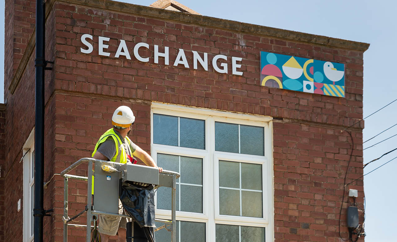 Nettl of Exeter team using a cherry picker to install the Seachange logo at Budleigh Hub.