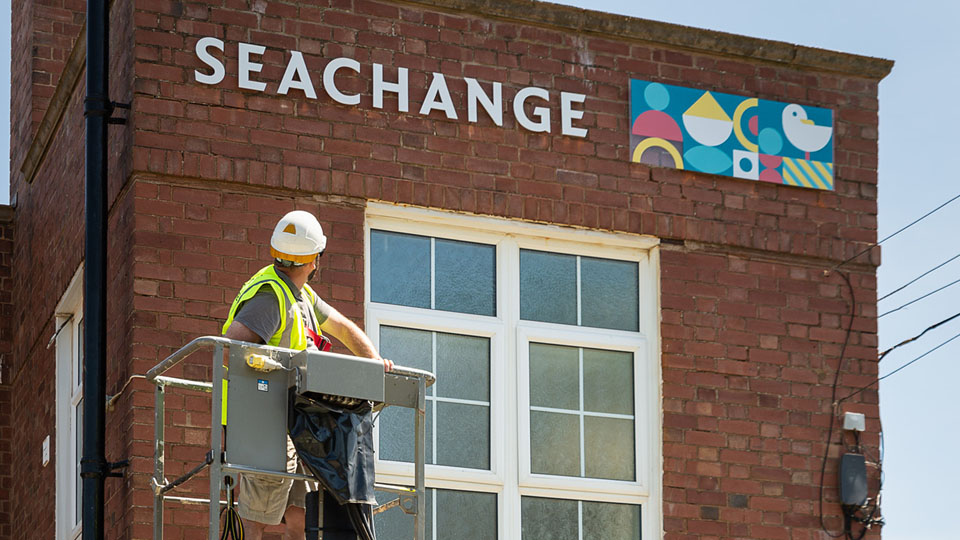 Nettl of Exeter using a cherry picker to install building signage at Seachange in Budleigh Salterton, Devon.